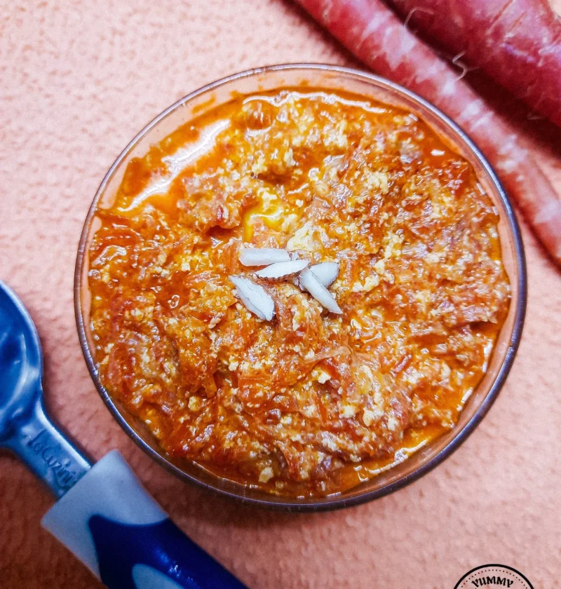 A bowl of rich, golden Gajar Ka Halwa topped with slivered almonds, exuding warmth and indulgence