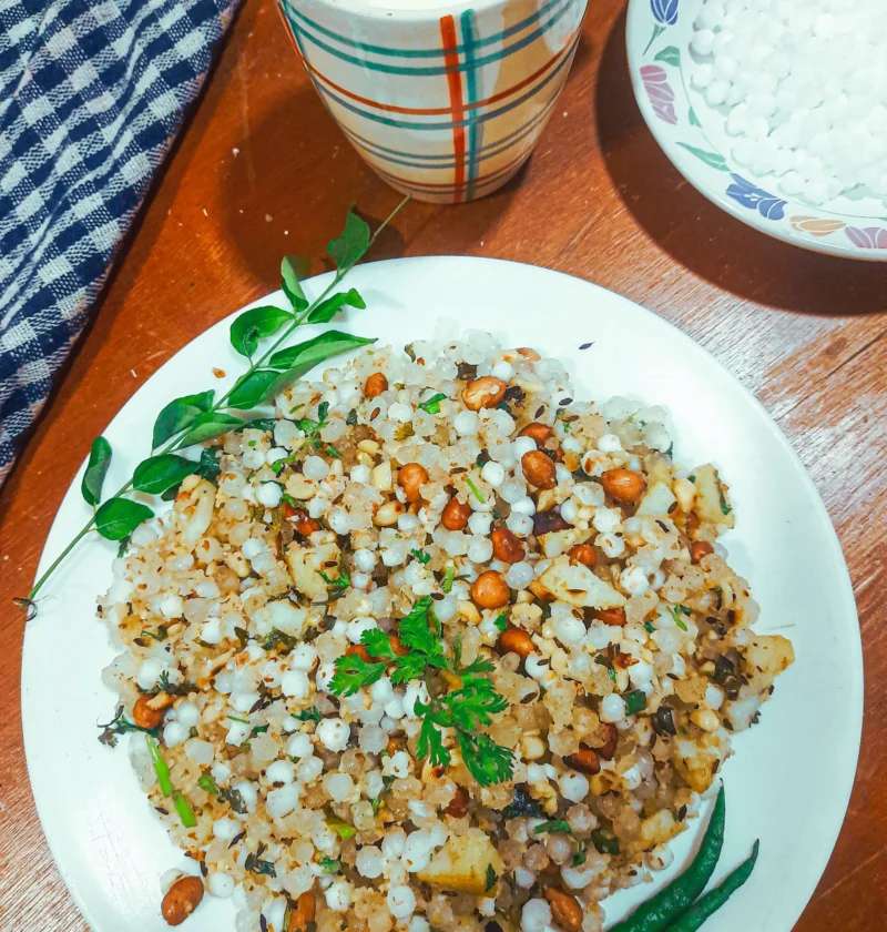 A plate of Sabudana khichdi for fast with fried chilies, accompanied by a cup of tea and a glass of milk.